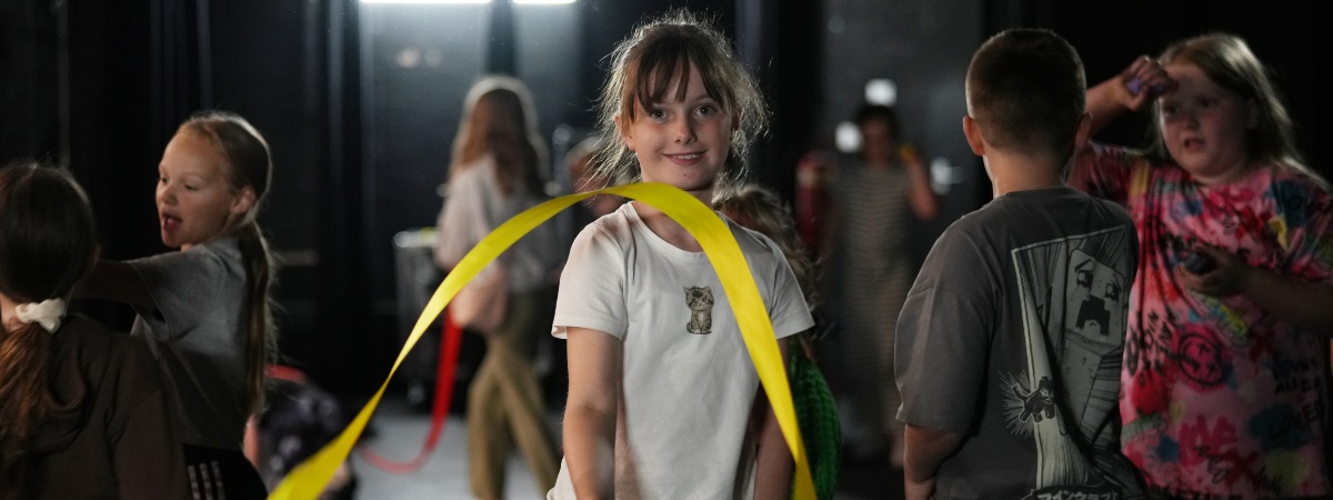 A young girl looks to camera whilst twirling a ribbon in an image for Empire Youth Theatre.