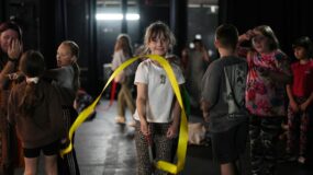A young girl looks to camera whilst twirling a ribbon in an image for Empire Youth Theatre.